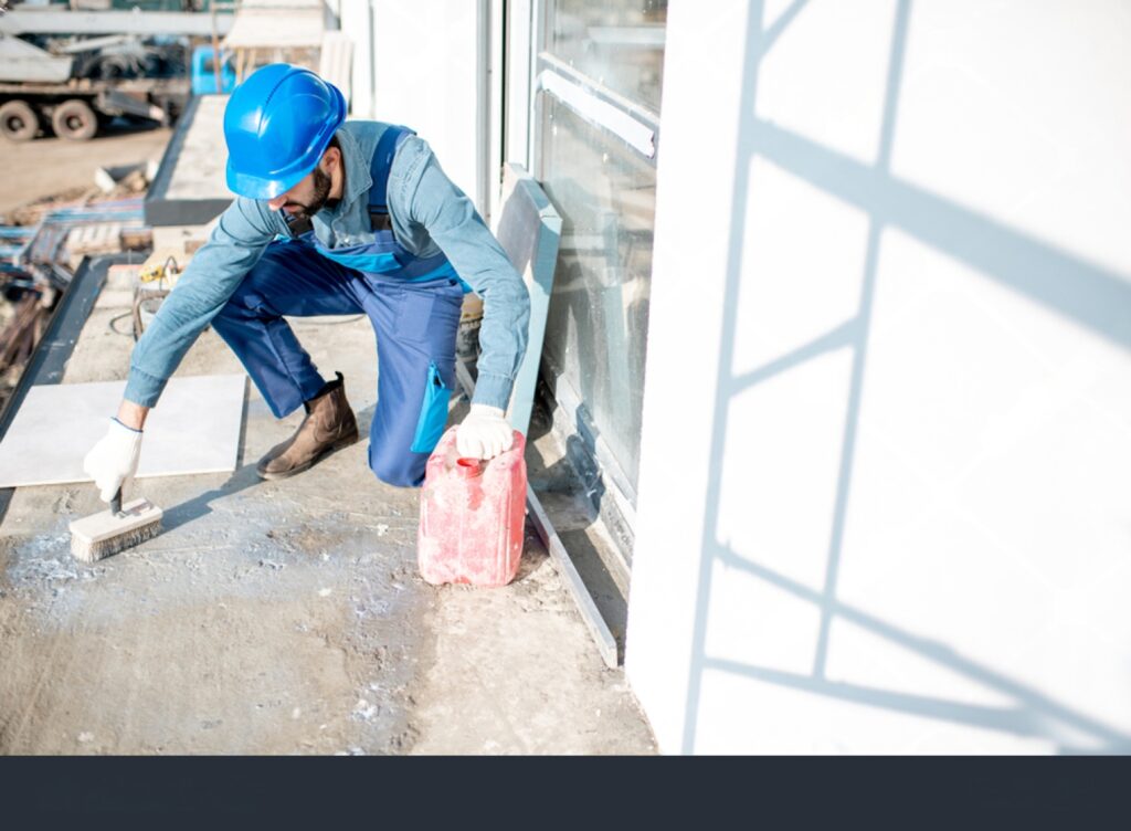 a construction worker applying a waterproofing coating to a floor.